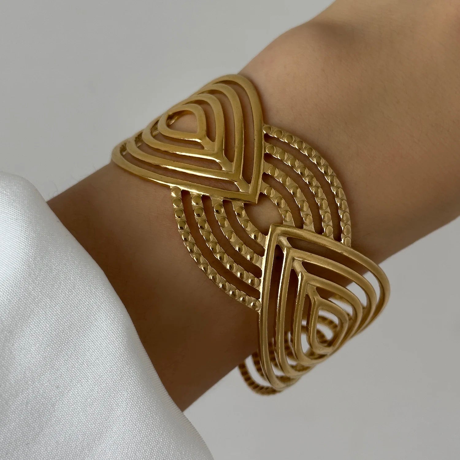Gold geometric cuff bracelet with layered triangular cut-out pattern, worn on wrist for a bold statement style