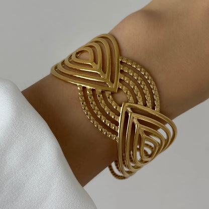 Gold geometric cuff bracelet with layered triangular cut-out pattern, worn on wrist for a bold statement style