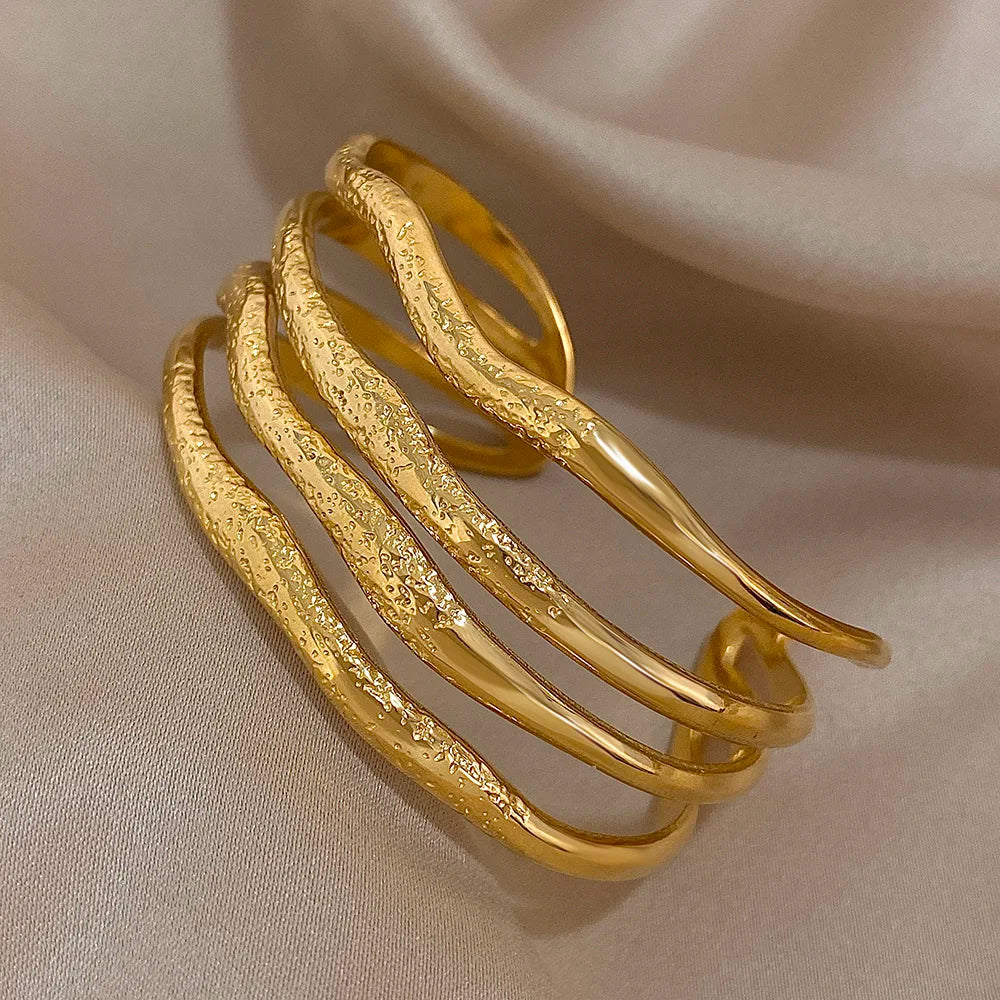 
Side view of a sculpted gold cuff bracelet with four curved textured bands