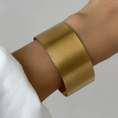 Wide gold cuff bracelet with smooth texture and minimalist open bangle design.