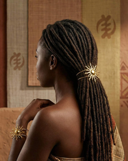 Woman with braided hair wearing a decorative hairpiece and bracelet in a warm-toned room.