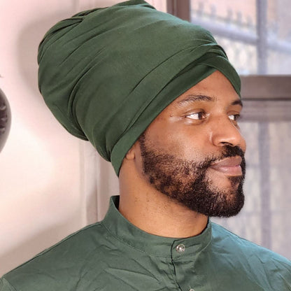 A man wearing a dark green turban and a matching green button-up shirt, shown in a close-up profile view against an indoor background.