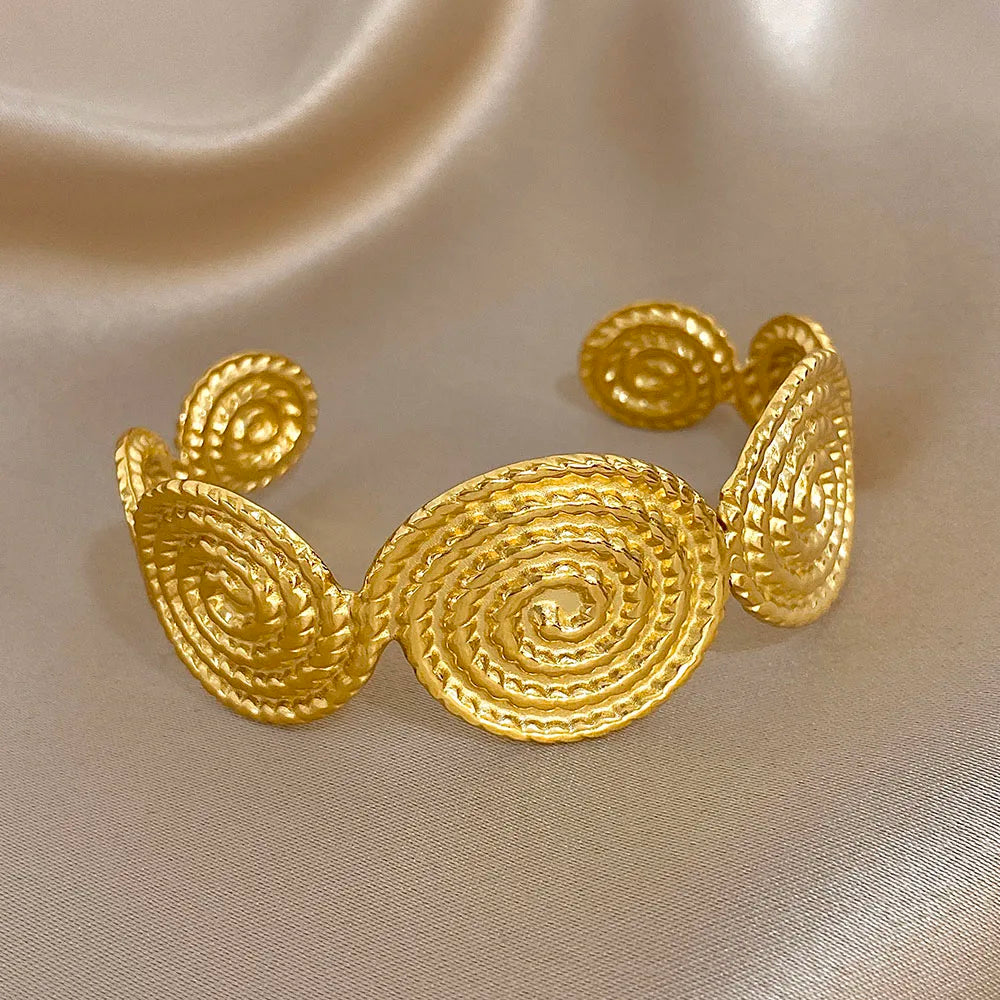 Gold spiral hair cuff with raised textured surface, displayed on a soft background.