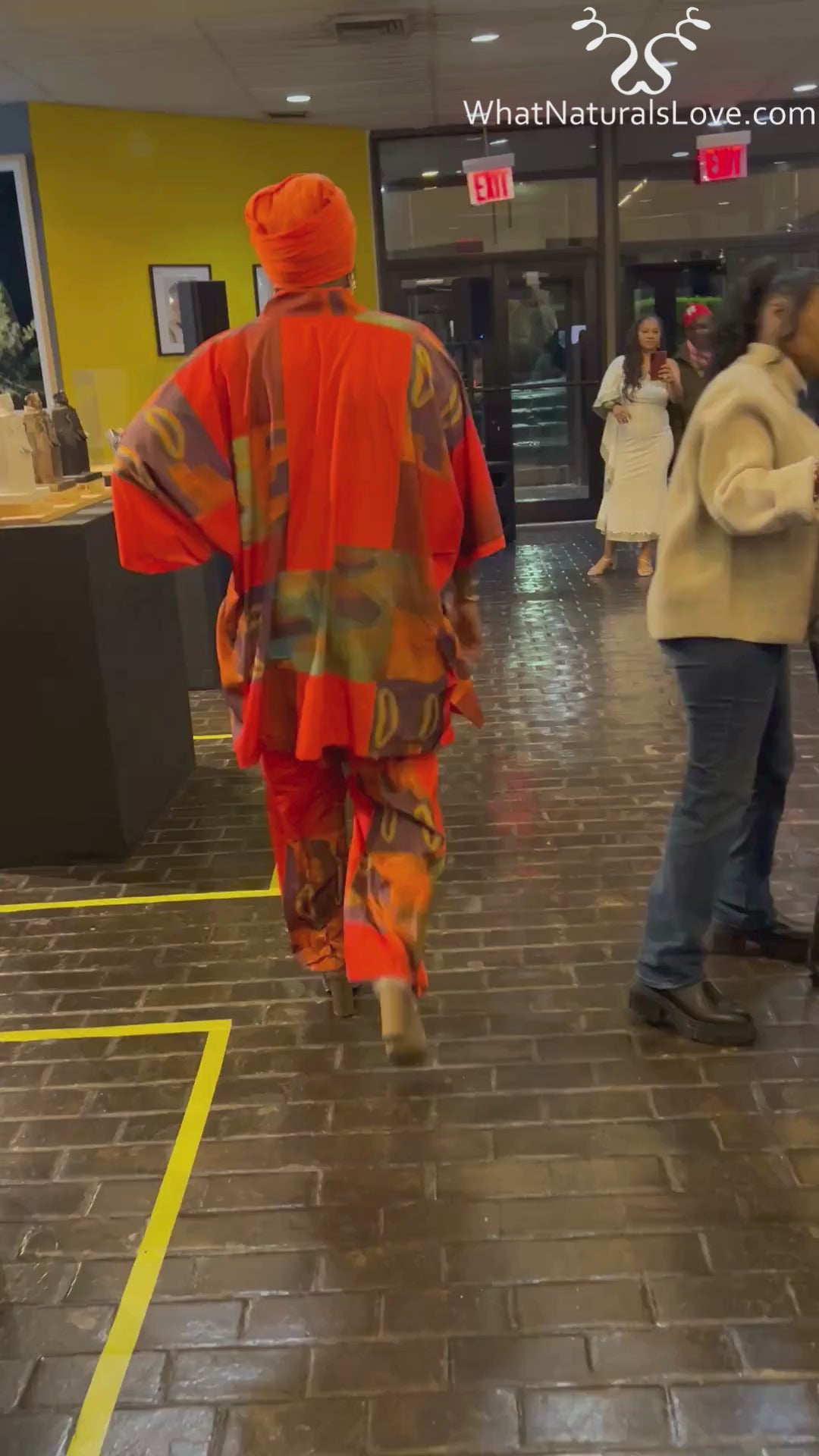 Vibrant African print pantset with matching headwrap, showcased at a fashion event. Bold red and orange tones with intricate patterns.