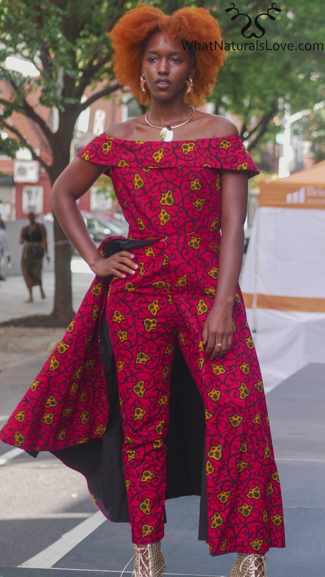 Stylish African pantsuit for women in vibrant red and yellow print. Off-shoulder design with flowing cape detail, perfect for business or casual wear.