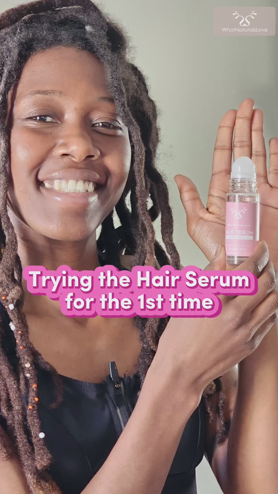 Smiling woman with locs holding What Naturals Love Hair Serum, trying it for the first time to promote scalp health and hydration.