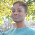 Woman with short natural hair wearing a teal sweater, showcasing healthy locs. Background features autumn foliage with soft lighting.